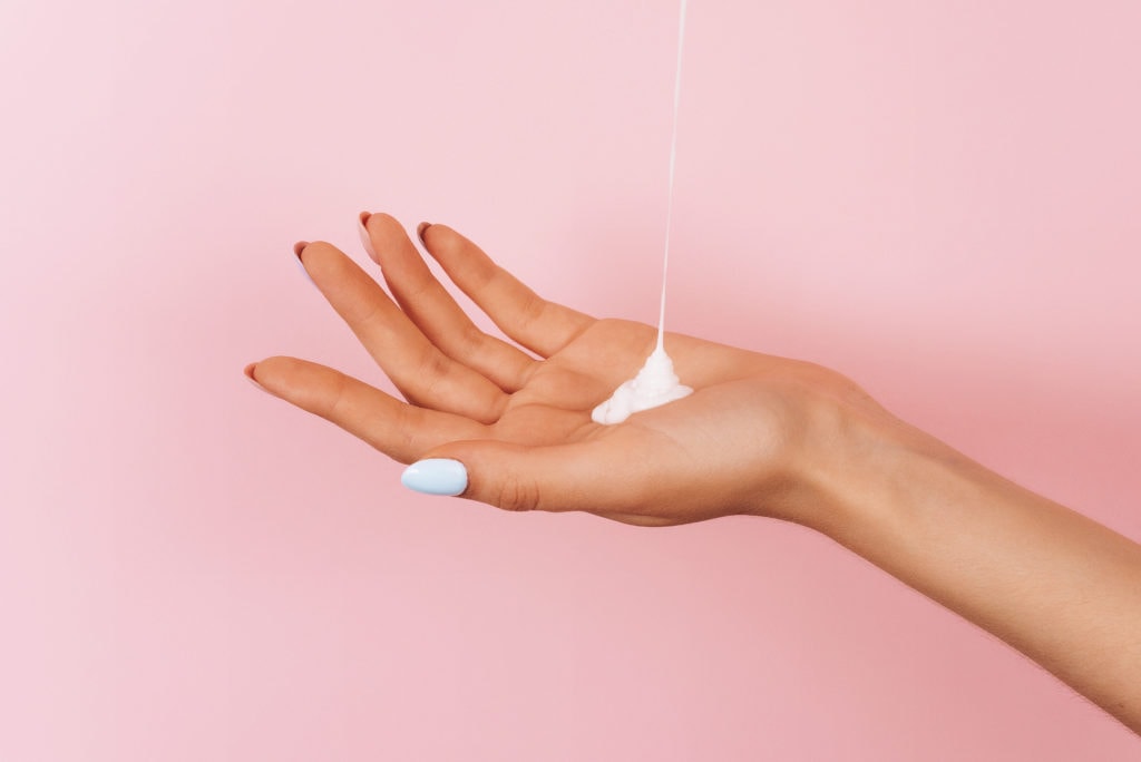 a stream of body cream pours onto a woman's hand. Skin moisturiz